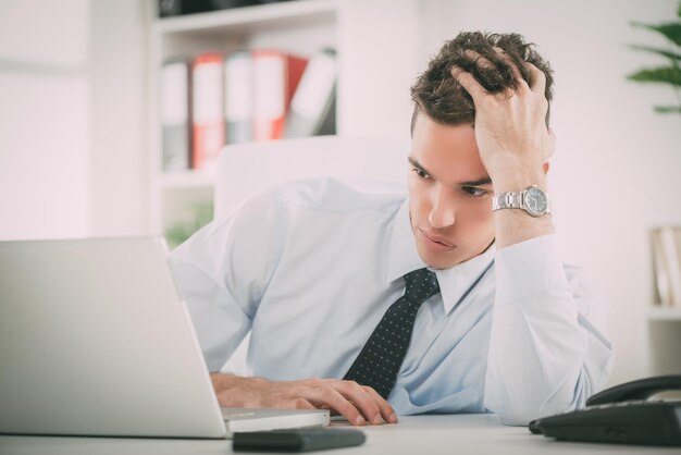 Empresario estresado en la oficina. Está preocupado, pensando y mirando en la computadora portátil.