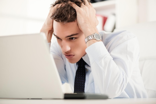 Empresario estresado sentado con una laptop en la oficina y pensando. Está preocupado y sosteniendo su cabeza con las manos.