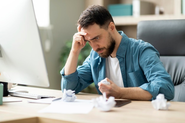 Empresário estressado com raiva amassando papel enquanto está sentado na mesa do escritório