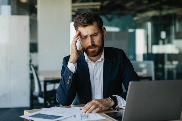 Empresário estressado sofrendo dor de cabeça sentado na mesa com muitos papéis empresário cansado com enxaqueca aguda