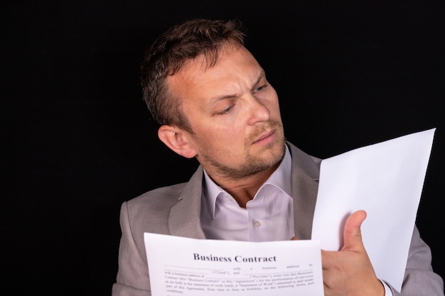 Empresário estudando um documento em papel com uma expressão séria enquanto está sentado em sua mesa no escritório