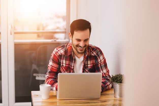 Empresario exitoso sonriendo con satisfacción mientras revisa la información de su computadora portátil mientras trabaja en una oficina en casa. Destello de lente