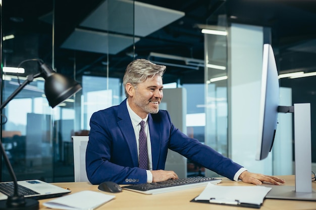 Foto empresário experiente de cabelos grisalhos trabalha no computador em um escritório moderno