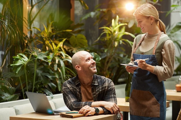 Empresário fazendo um pedido para o garçom enquanto trabalhava com o laptop na mesa de um café