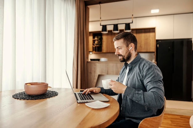 Un empresario feliz disfruta de su café mientras trabaja desde casa en una computadora portátil