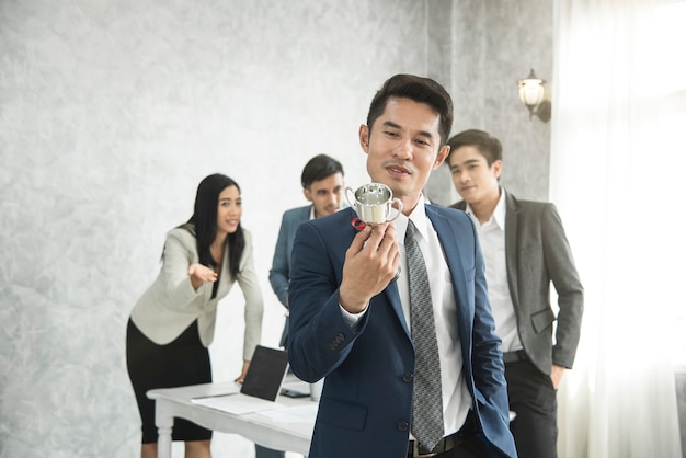 empresario feliz orgullo con Copa de ganar y equipo de negocios celoso detrás