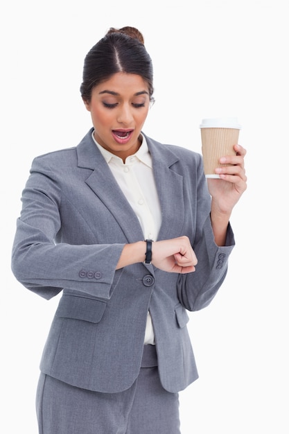 Empresario femenino sorprendido con taza de papel mirando su reloj