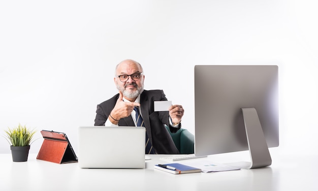 Empresário financeiro sênior indiano asiático, sentado em sua estação de trabalho ou mesa na frente de um computador, laptop e tablet. falar ao telefone enquanto cuida da papelada