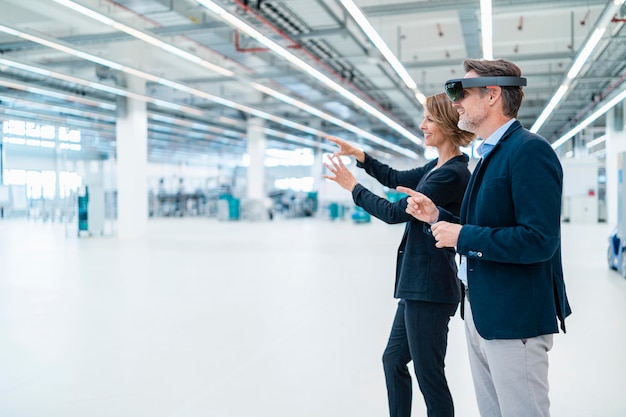 Empresario con gafas AR y empresaria en una sala de fábrica