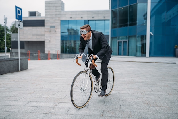 Un empresario con gafas divertidas posa en bicicleta en el edificio de oficinas en el centro de la ciudad. Persona de negocios en transporte ecológico en las calles de la ciudad