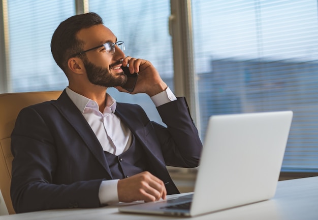 El empresario de gafas sentado en el escritorio y llamando