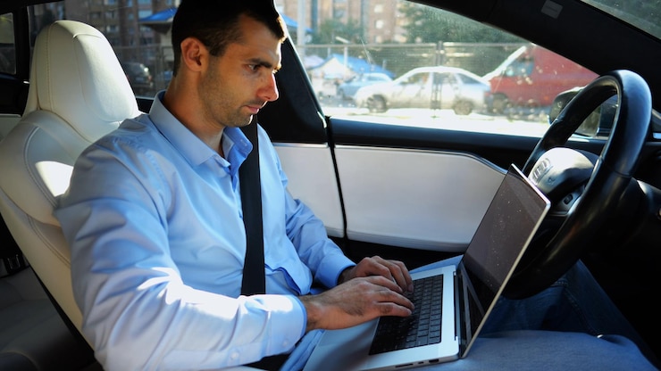 Foto empresario guapo trabajando en un portátil mientras conduce un automóvil eléctrico autónomo en una carretera urbana empresario masculino escribiendo texto en su portátil mientras viaja en un vehículo eléctrico con piloto automático