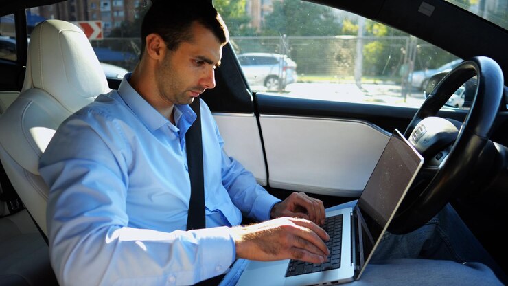 Foto empresario guapo trabajando en un portátil mientras conduce un automóvil eléctrico autónomo en una carretera urbana empresario masculino escribiendo texto en su portátil mientras viaja en un vehículo eléctrico con piloto automático
