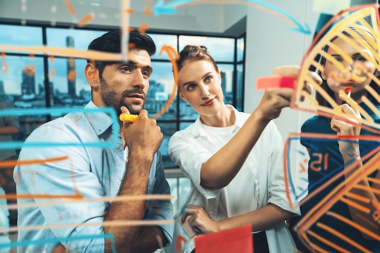 Foto un empresario hábil sonriente escribiendo un gráfico en una pared de vidrio para un compañero de trabajo.