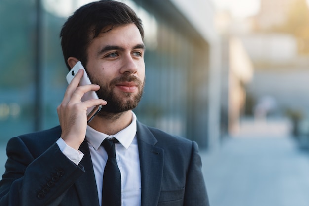 Empresario hablando por teléfono inteligente contra el edificio de negocios al aire libre