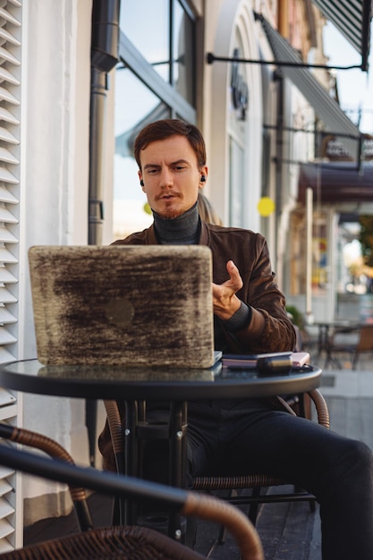 Empresario hablando por videollamada a través de una computadora portátil mientras trabaja en un proyecto de forma remota en un café en la ciudad