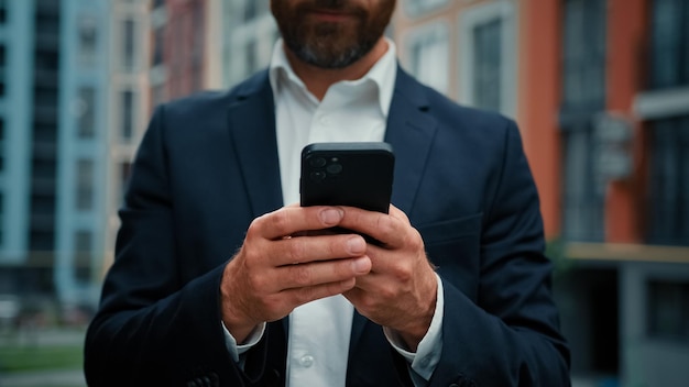 Empresario hombre desconocido parado en la ciudad mantenga teléfono gadget enviar mensajes comunicación virtual hacer