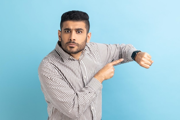 Empresario impaciente con barba apuntando con el dedo al reloj de pulsera y luciendo molesto y disgustado