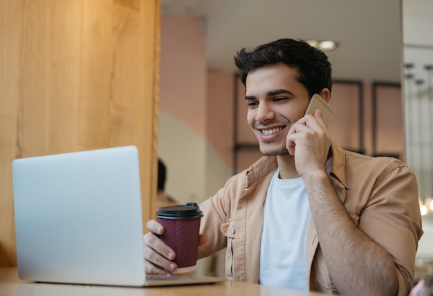 Empresário indiano bonito falando no celular, segurando a xícara de café, trabalhando em casa