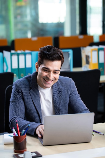 Empresário indiano visionário sorrindo enquanto digita no teclado do laptop