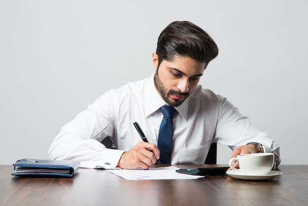 Empresario indio escribiendo un documento mientras está sentado en un escritorio o estación de trabajo