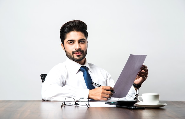 Empresario indio escribiendo un documento mientras está sentado en un escritorio o estación de trabajo