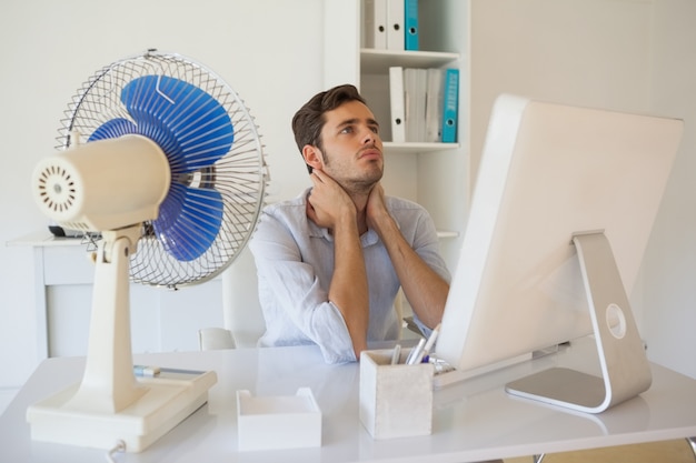 Empresario informal sentado en el escritorio con ventilador eléctrico