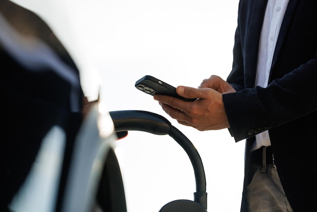 Empresário irreconhecível, desconectando o carro elétrico da estação de carregamento, carregando o carro elétrico masculino