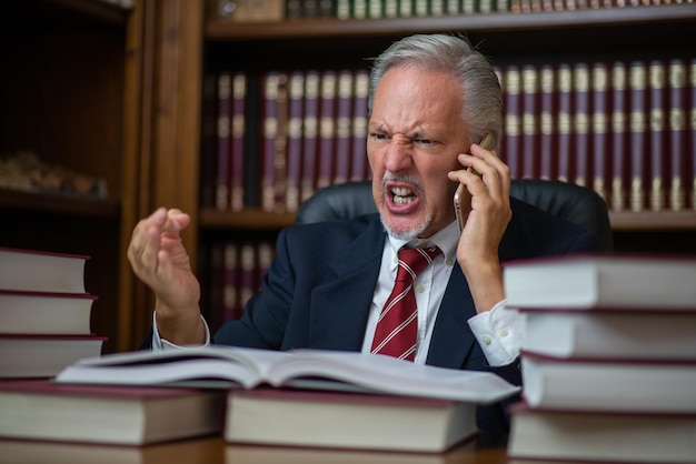 Empresário irritado falando no celular e lendo um livro