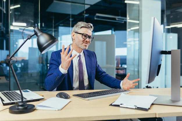 Empresario jefe enojado y molesto gritando a un monitor de computadora con gafas trabajando en una oficina moderna en la computadora