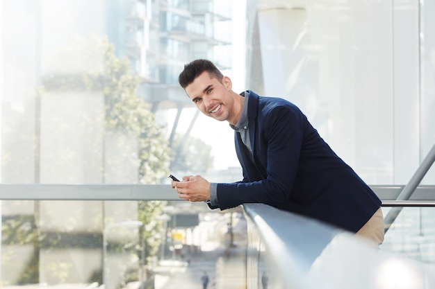 Empresário jovem sorridente permanente com telefone inteligente