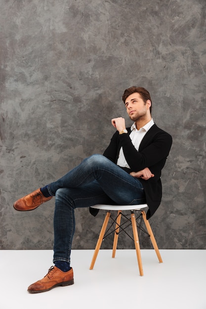 Foto empresario joven pensativo sentado sobre pared gris