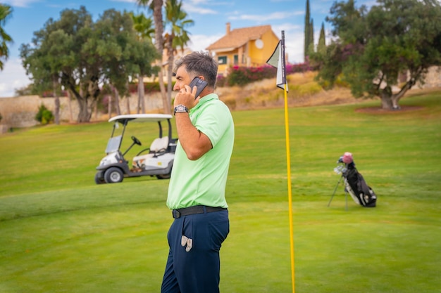 Empresario jugando al golf y respondiendo una llamada de trabajo con el teléfono del club