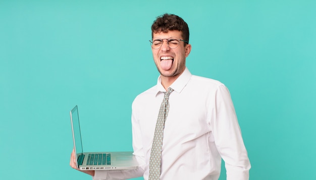 Empresario con laptop con actitud alegre, despreocupada y rebelde, bromeando y sacando la lengua, divirtiéndose