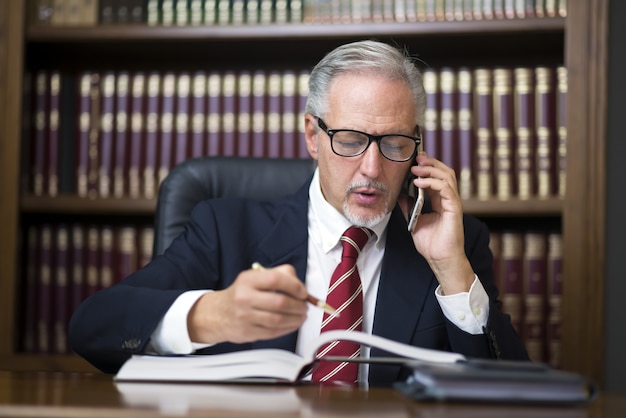 Empresario leyendo un libro mientras habla por su teléfono móvil