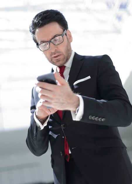 Empresario leyendo un mensaje de texto en el teléfono inteligente mientras está de pie en la oficina