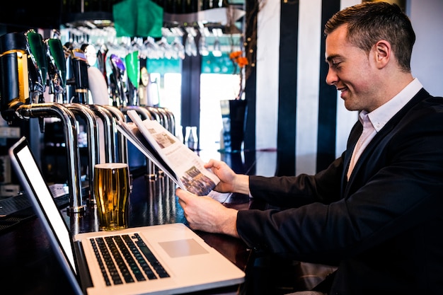 Foto empresario leyendo las noticias y usando la computadora portátil en el mostrador de un bar