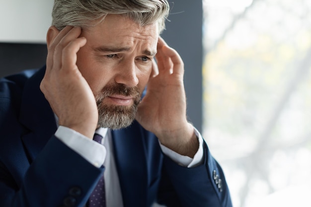 Empresário maduro chateado sofrendo dor de cabeça aguda no local de trabalho no escritório