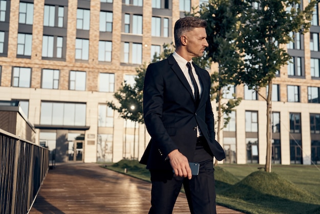 Empresário maduro confiante caminhando ao ar livre com um prédio de escritórios ao fundo