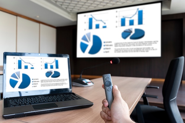 Foto el empresario mantenga la diapositiva de control remoto con la presentación del gráfico simulado en la pantalla y la computadora portátil