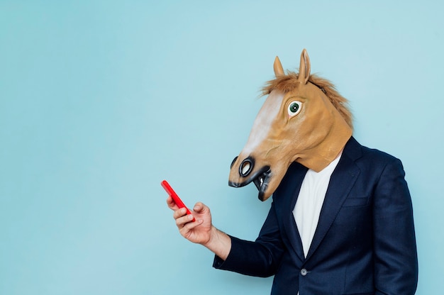 Foto empresario con máscara de caballo con smartphone