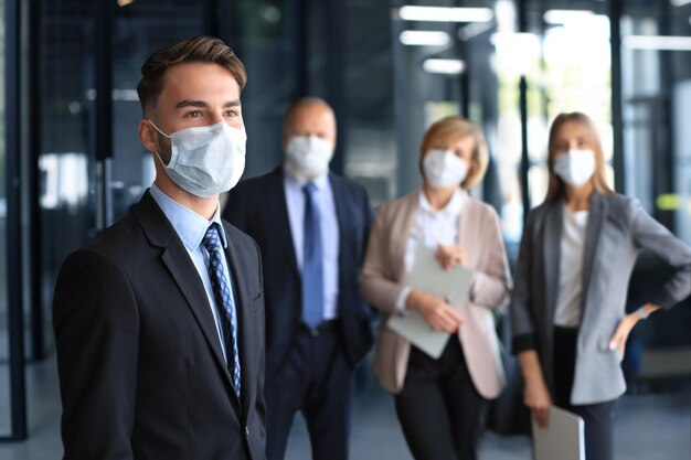 Foto empresario con máscara médica con colegas en segundo plano en el cargo.