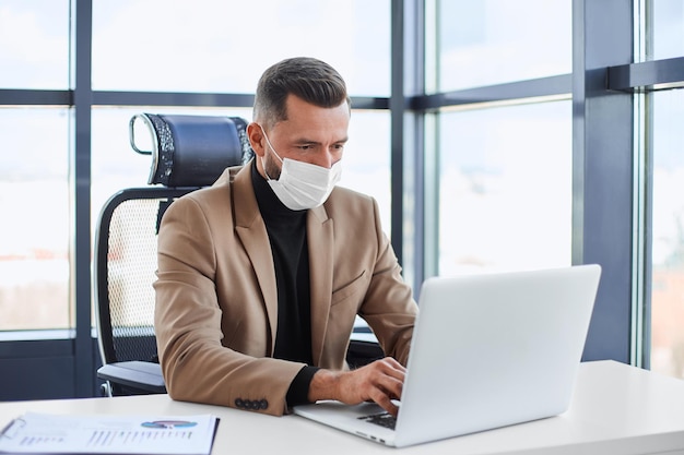 Empresario con una máscara protectora trabajando en una computadora portátil