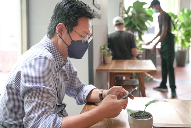 Empresario con mascarilla al usar su teléfono en un restaurante