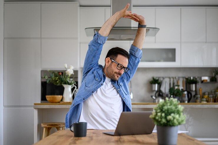 Foto empresario masculino cansado que estira los brazos mientras trabaja horas extras en una computadora portátil en el escritorio de la oficina en casa