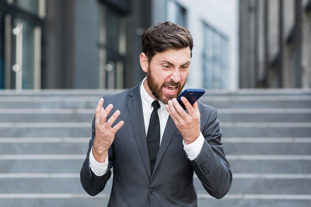 Empresário masculino com raiva chora falando ao telefone do lado de fora do homem de negócios, gritando de plantão ao ar livre. Nervosa conversa profissional louca no smartphone. Grito de funcionário irritado fala na rua urbana