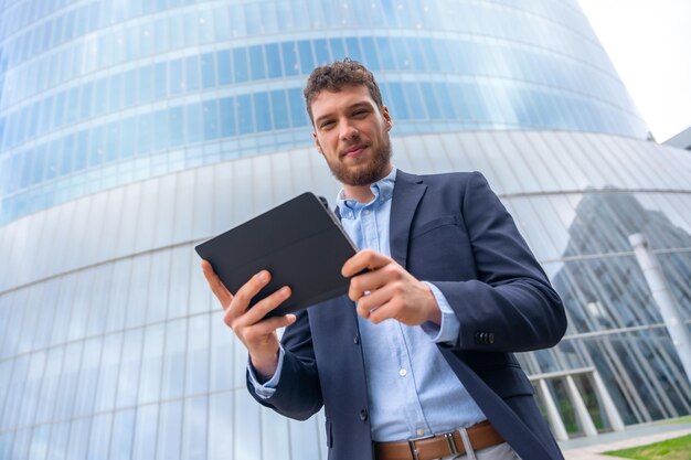 Empresário masculino de retrato ou empresário fora do escritório usando um tablet em um prédio de vidro