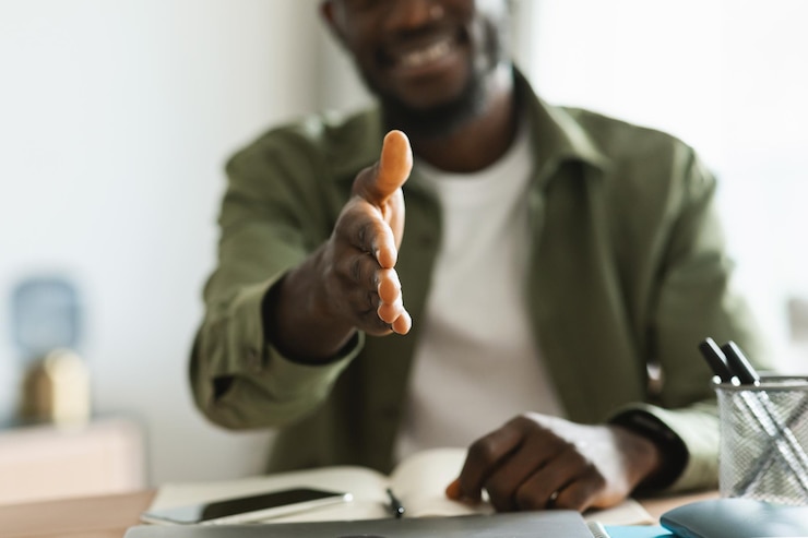 Foto empresario masculino negro que extiende la mano para un apretón de manos en la cámara que ofrece asociación sentado en el enfoque selectivo de la oficina