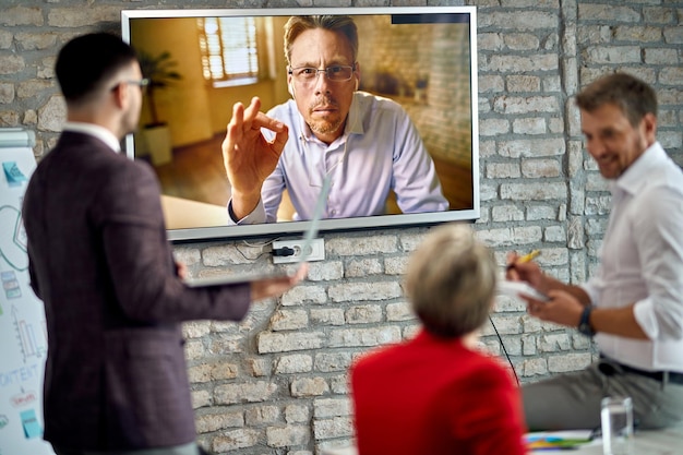 Empresario masculino que se une a una reunión de negocios a través de una videoconferencia y habla con sus compañeros de trabajo en la oficina