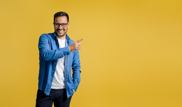 Empresario masculino sonriente apuntando al espacio de copia para marketing mientras está de pie sobre fondo amarillo